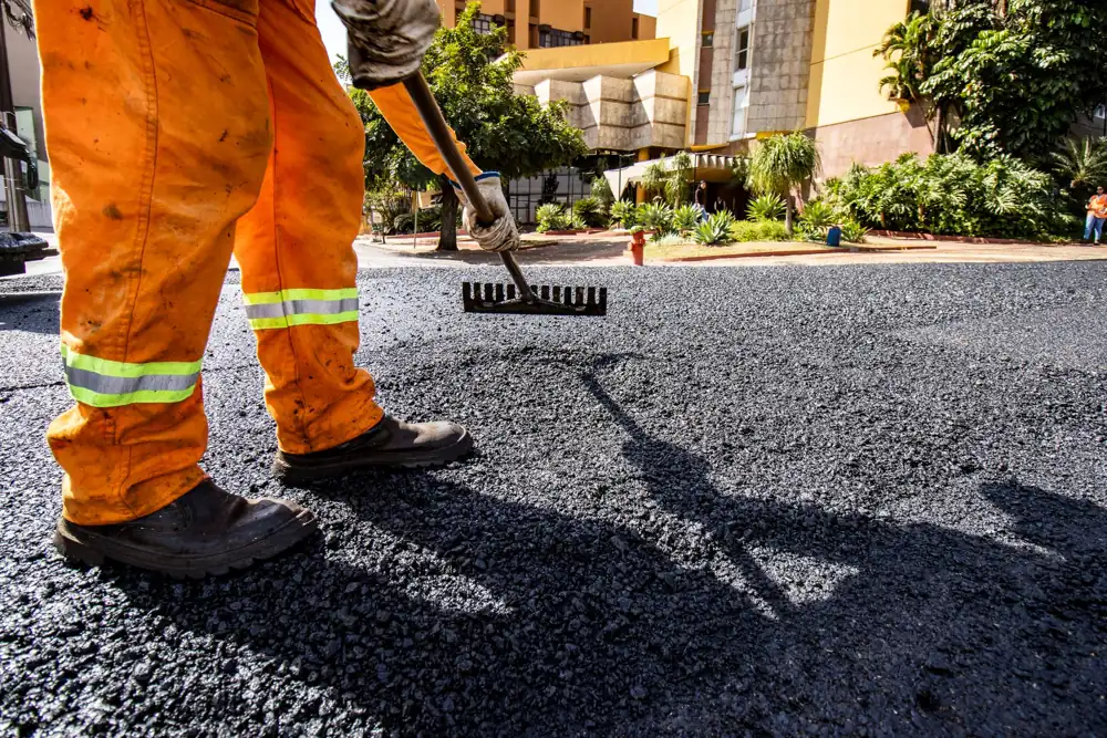 Worker raking hot asphalt into place